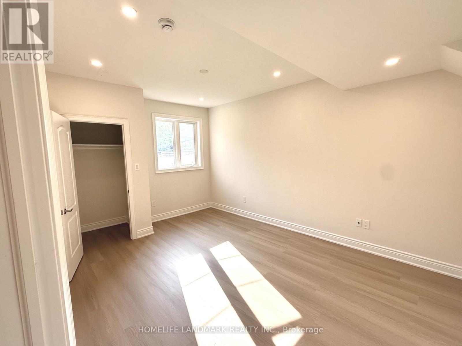 A spacious room with wooden flooring and a window letting in natural light.
