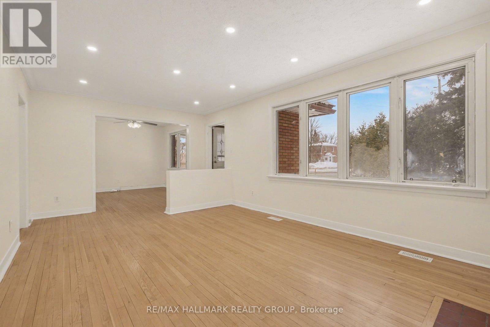 A room with wooden flooring and white walls, with a window showing a tree and a building outside.