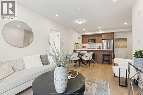 A modern living room with a grey sofa, a round table with a vase on it, and a kitchen area in the background.