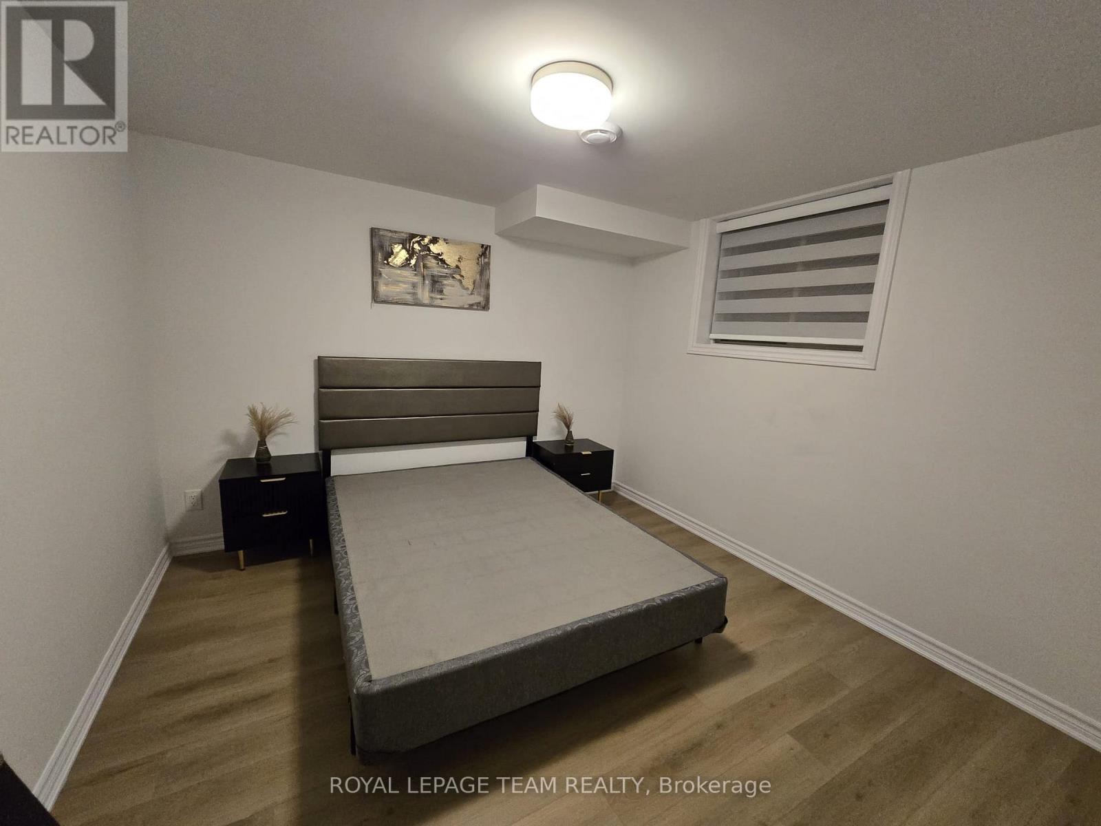 A bedroom with a bed, wooden floor, and white walls.
