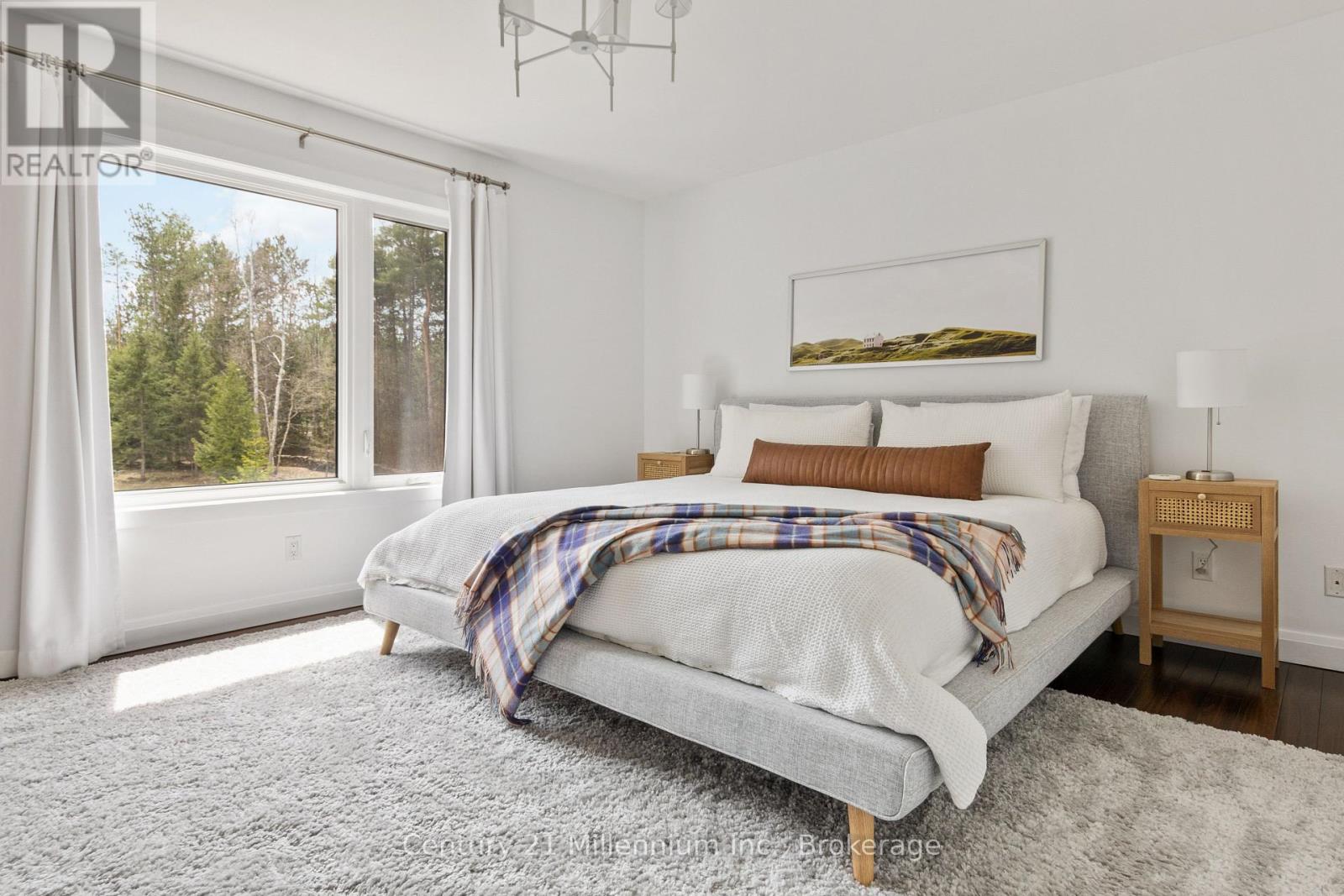 A bedroom with a large bed and a view of trees outside the window.