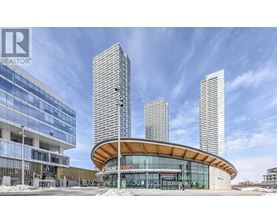 A modern building with a curved glass entrance and three tall towers in the background.