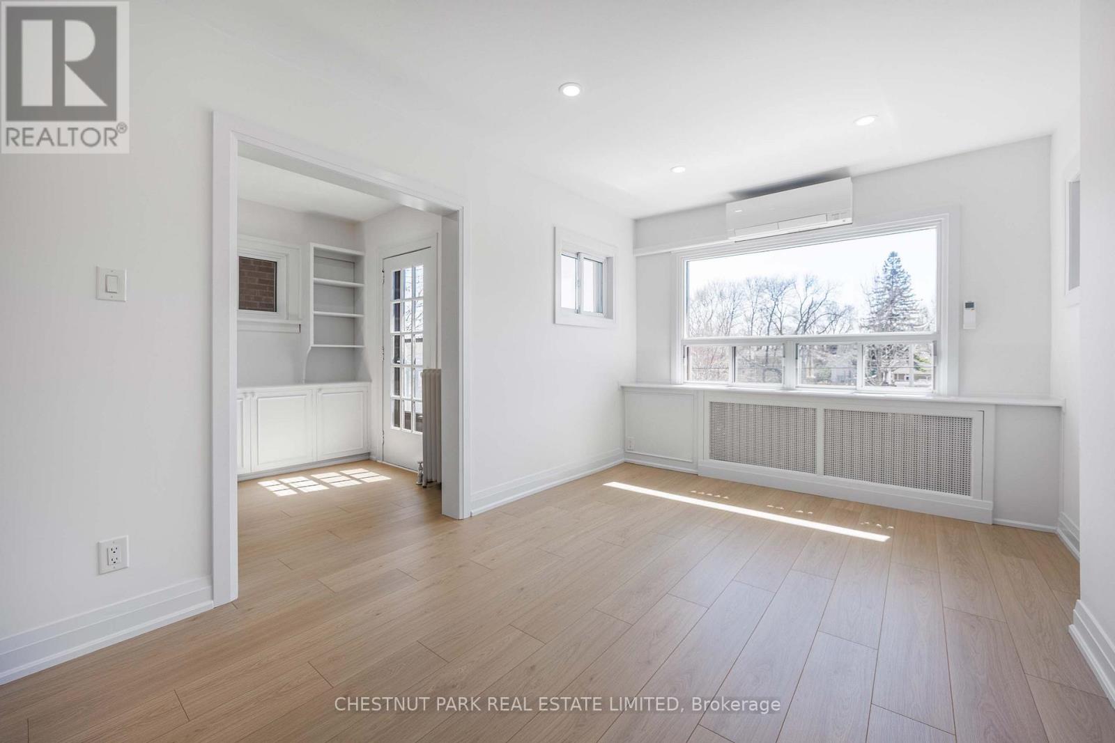 A spacious room with wooden flooring and a large window.