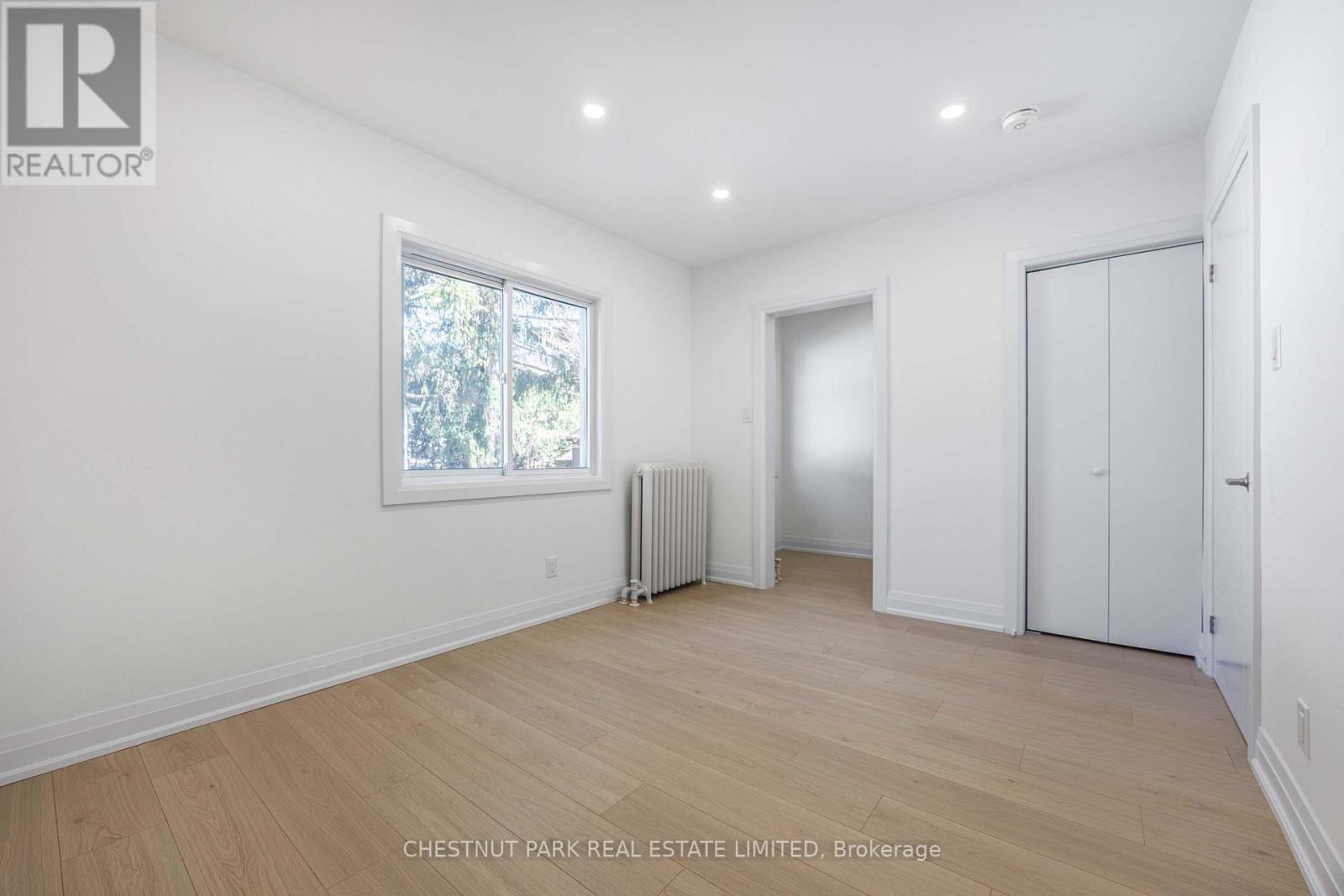 A white room with wood flooring and a window with a view of trees outside.