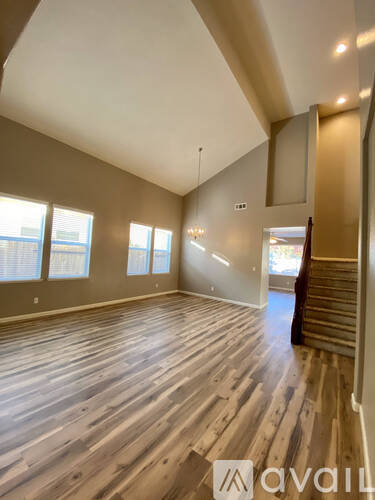 A spacious room with wooden flooring and a staircase on the right side.