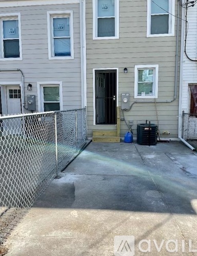 A concrete patio in front of a house with a fence and a black trash can.