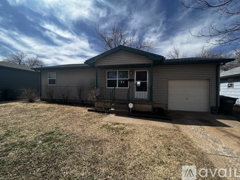A house with a grey siding and a white garage door is surrounded by a grassy area.
