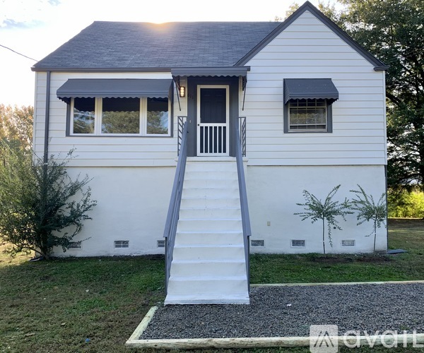 A small white house with a black roof and a grey staircase leading to the front door.