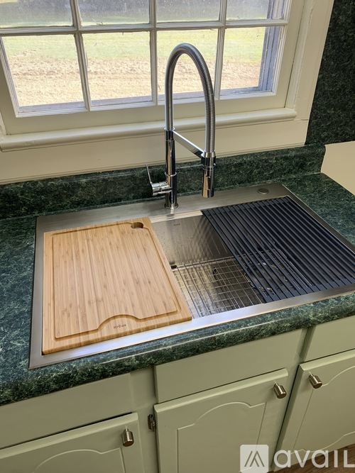 A kitchen sink with a wooden cutting board on the counter.