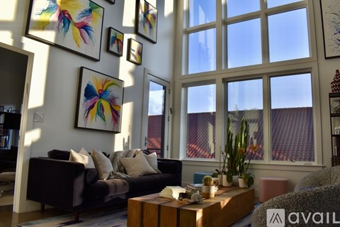 A living room with a black couch, a coffee table, and several paintings on the wall.