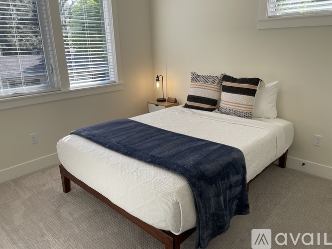 A bedroom with a neatly made bed and a window with blinds.