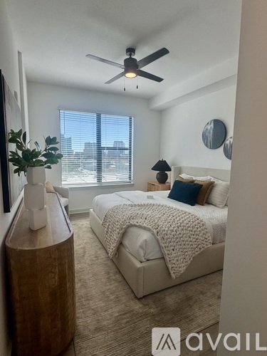 A bedroom with a bed, a ceiling fan, and a window with a view of the city.