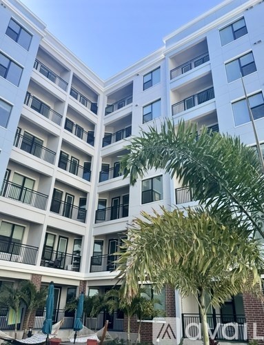 A tall white building with balconies and a tree in front.