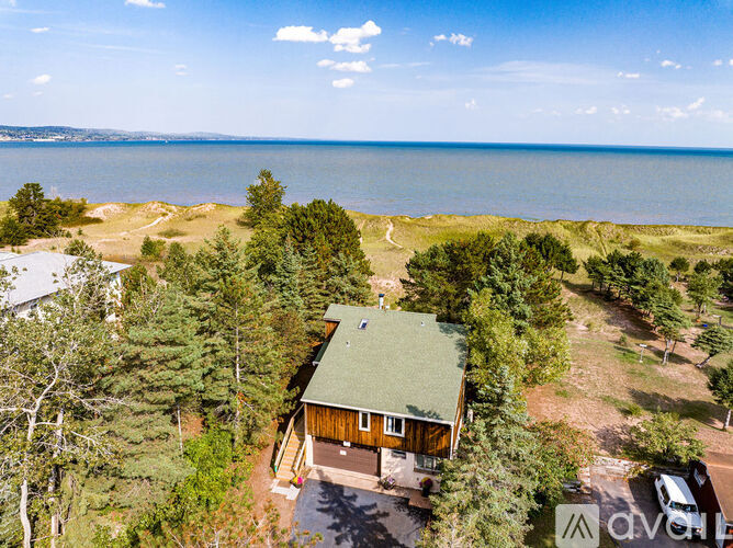 A house with a green roof is surrounded by trees and is located near a body of water.