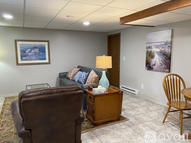 A living room with a brown leather chair, a wooden table with a lamp and a picture on the wall.