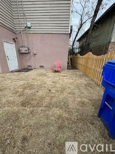 A backyard with a pink chair and a blue dumpster.
