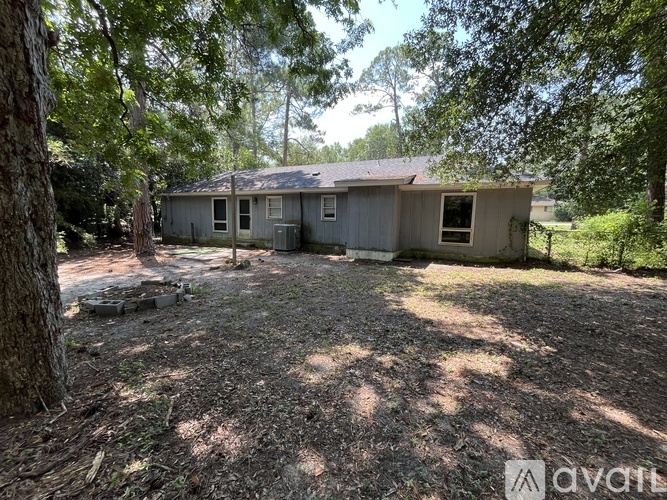 A small, dilapidated house sits in a backyard surrounded by trees.