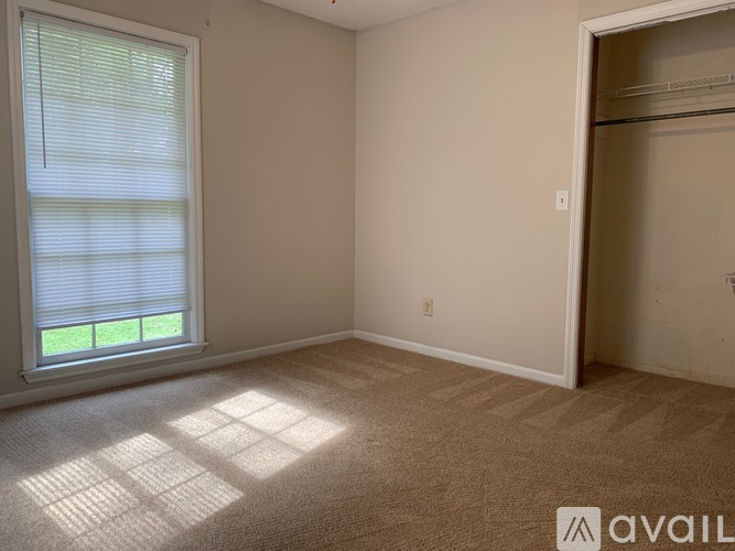 A room with a carpeted floor, a window with blinds, and a door leading to another room.