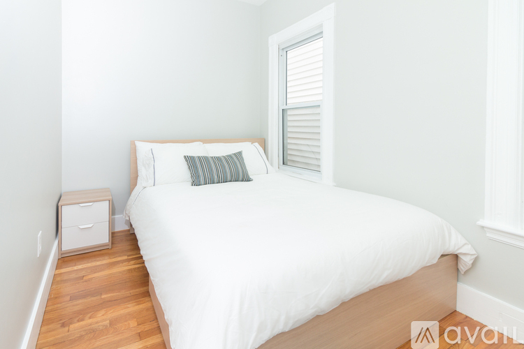A bed with a white comforter and a striped pillow is in a room with a wooden floor and white walls.