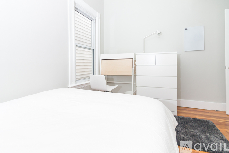 A white bedroom with a bed, nightstand, and lamp.