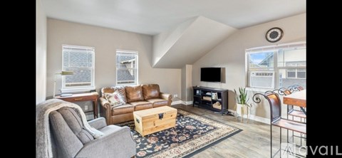 A living room with a grey couch, a brown leather couch, a wooden coffee table, a television, and a large window.