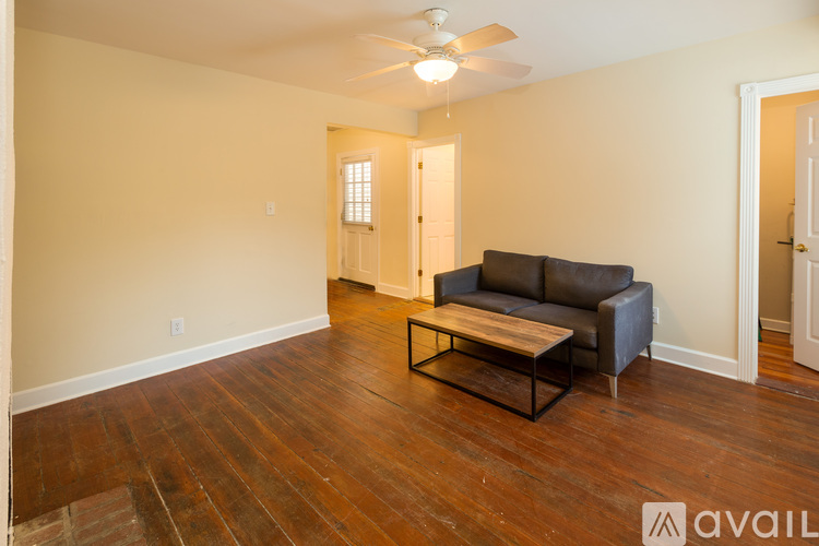 A living room with a black leather couch and wooden floors.