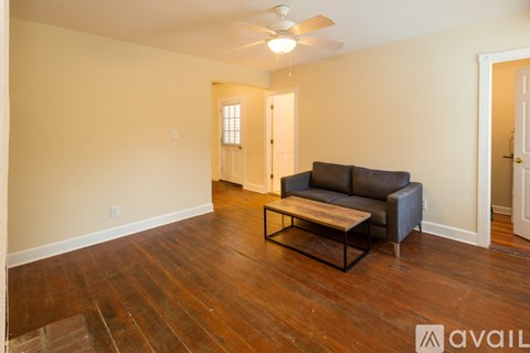 A living room with a black leather couch and wooden floors.