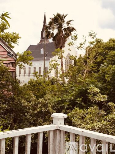 A white wooden fence in the foreground with a church and palm trees in the background.