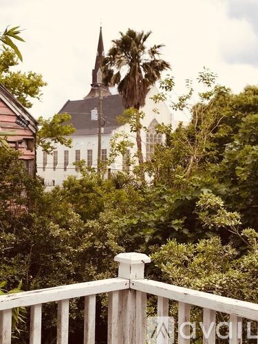 A white wooden fence in the foreground with a church and palm trees in the background.