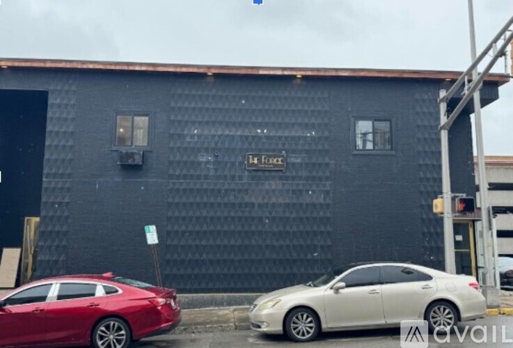 A red car is parked in front of a black building with a sign that reads "La Faction.".
