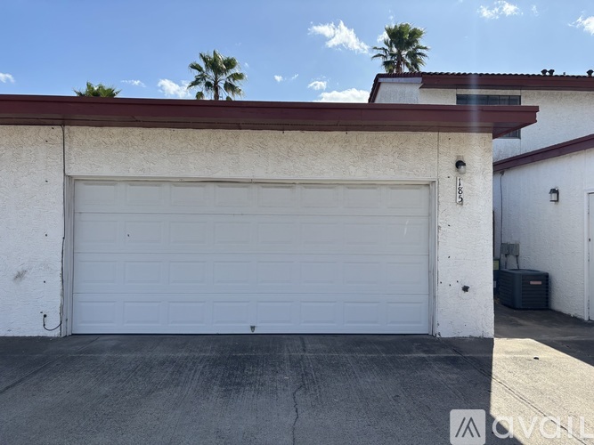 A white garage door is closed and there is a wall on the left side of the garage.