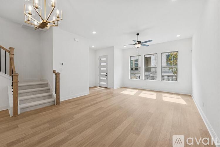 A spacious room with wooden flooring and a staircase with a chandelier.
