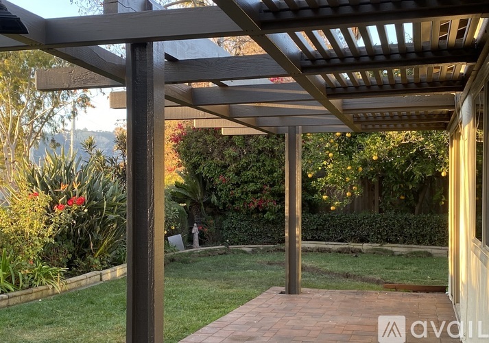 A patio with a wooden pergola and brick walkway.