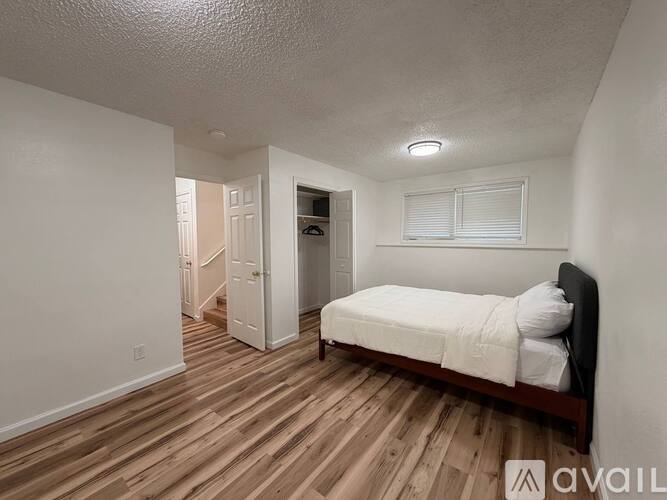 A bedroom with a bed, wooden floors, and a white door.