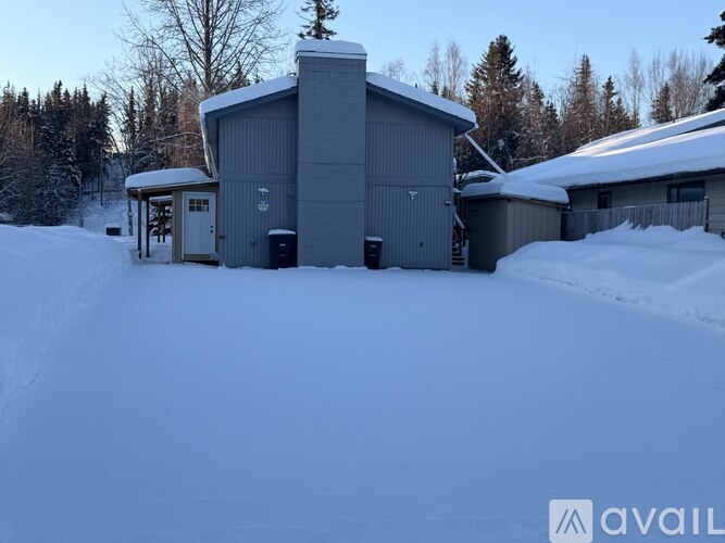 A snow-covered ground with a building and trees in the background.
