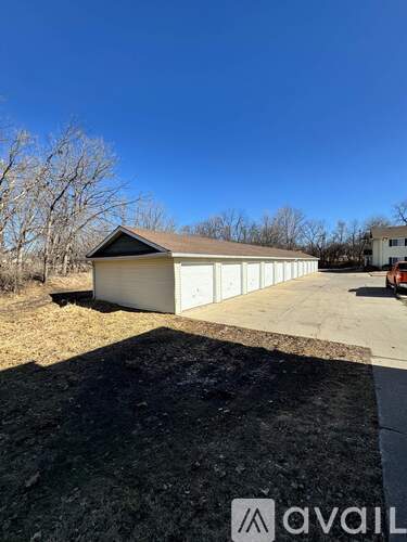 A large white garage with a brown roof is situated in a grassy area with a clear blue sky above.