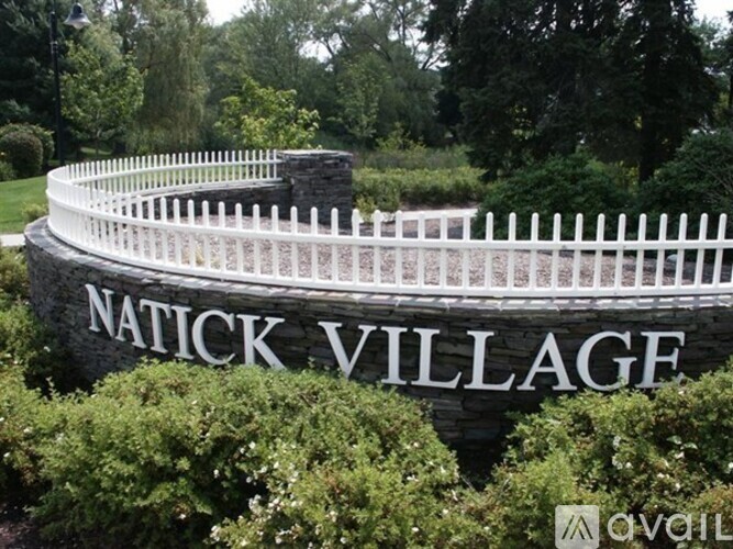 A white picket fence surrounds a sign that says Natick Village.