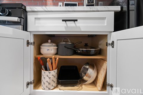 A kitchen cabinet is open, revealing pots, pans, and utensils.