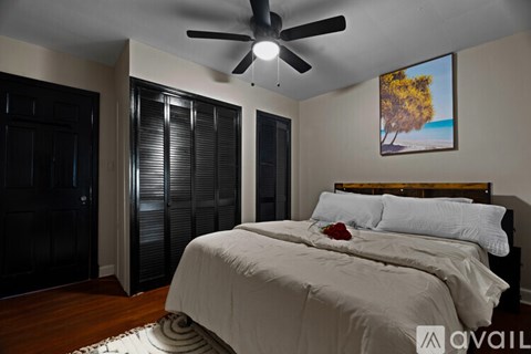 A bedroom with a bed, a ceiling fan, and a painting of a tree.