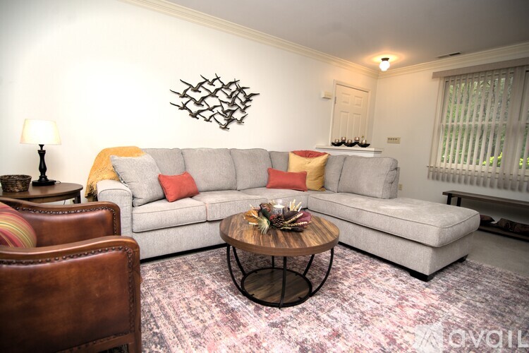 A living room with a grey couch, a brown leather chair, and a coffee table with a vase on it.