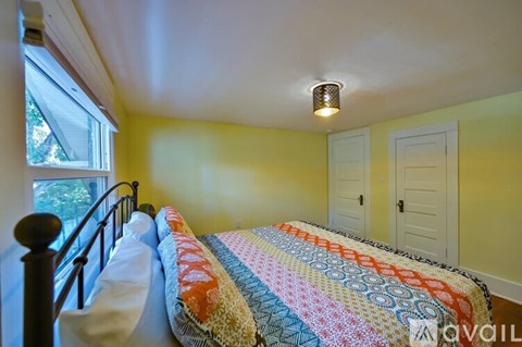 A bedroom with a bed covered in a quilt and a window with a view of trees.