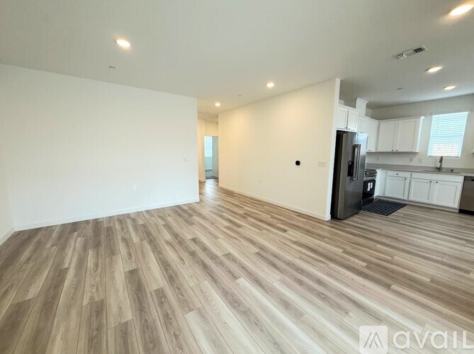 A spacious room with wooden flooring and a kitchen area in the background.