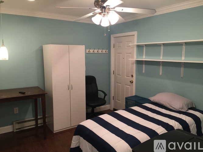A bedroom with a bed, desk, chair, and a ceiling fan.