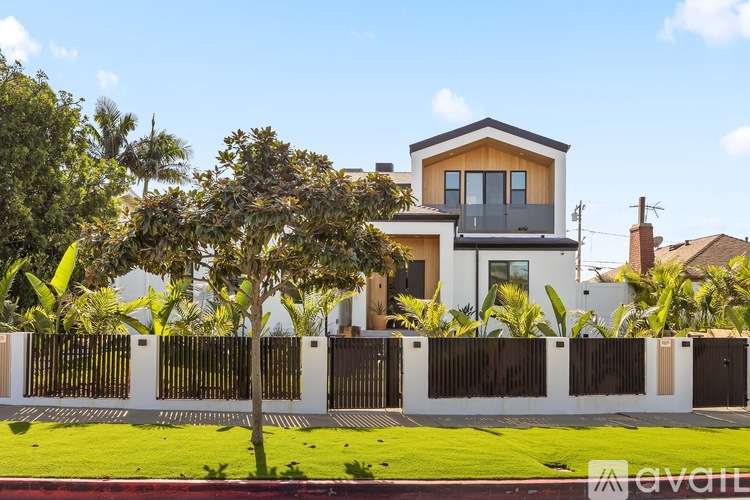 A modern house with a white fence and a tree in front.