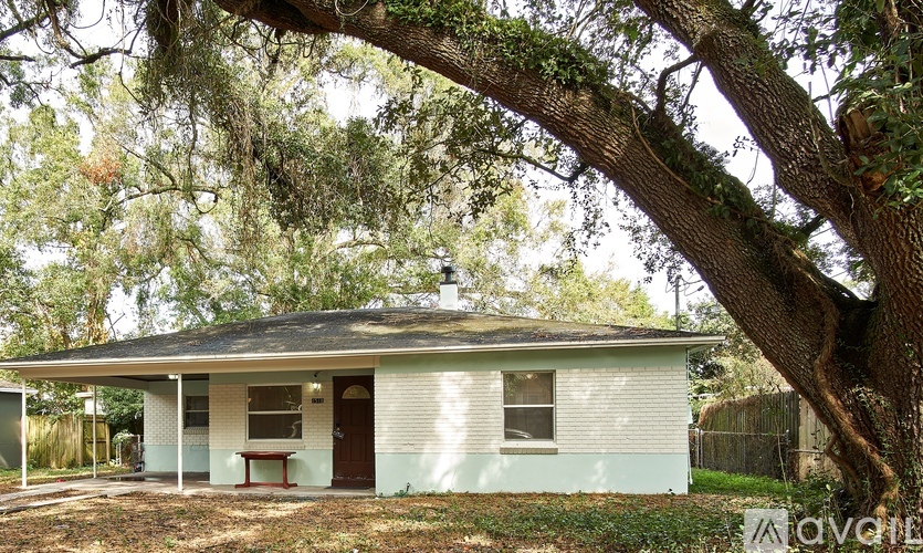 A white house with a porch and a tree in front.