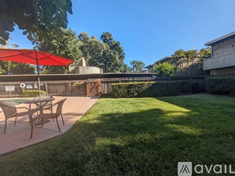 A backyard with a table and chairs under a red umbrella.