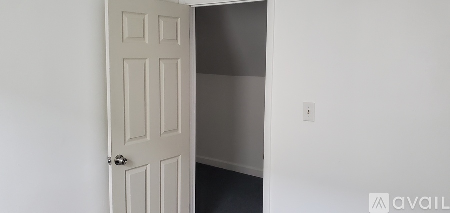 A white door with a silver handle is open to a dark hallway.