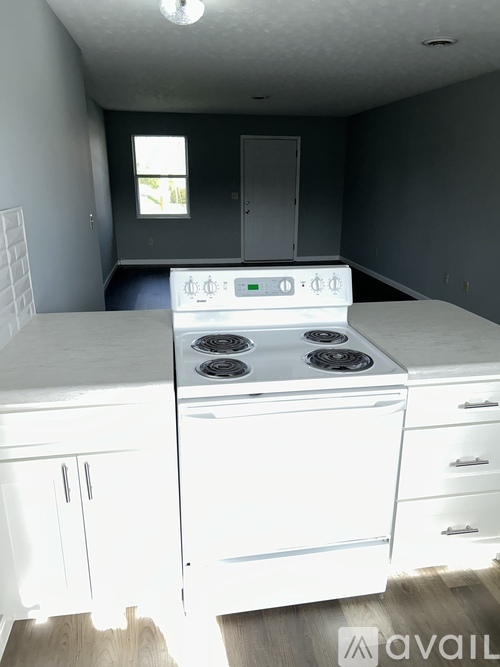 A white stove top oven with four burners and a white counter top with a window above it.