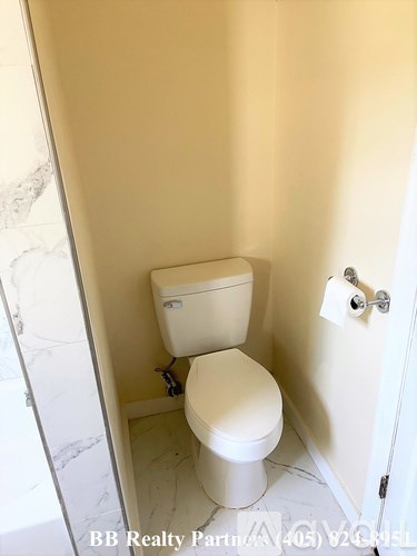 A white toilet in a small bathroom with a roll of toilet paper on the wall.