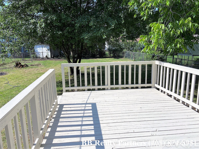 A white deck with a railing and trees in the background.